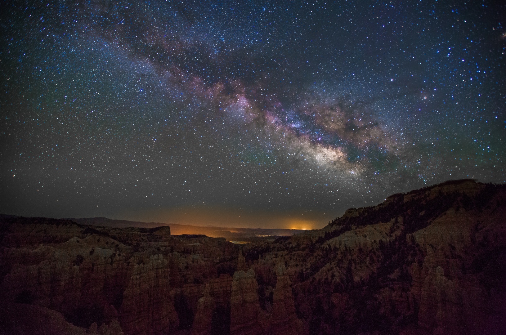 A night photo showing the Milky Way in the sky, with mountains in the foreground